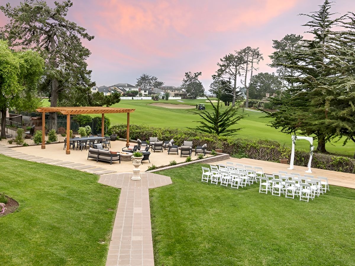 Outdoor wedding venue with a stone walkway, lined white chairs, and manicured lawns under sunset skies.